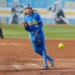 A UCLA softball pitcher in a blue uniform with yellow lettering pitches a neon yellow softball.