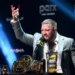 Conor McGregor speaking at a boxing news conference with a championship belt and products on a table in front of him.