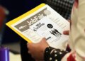 A person holding a flyer for a job fair with "Job Fair" and "Help Wanted" visible.