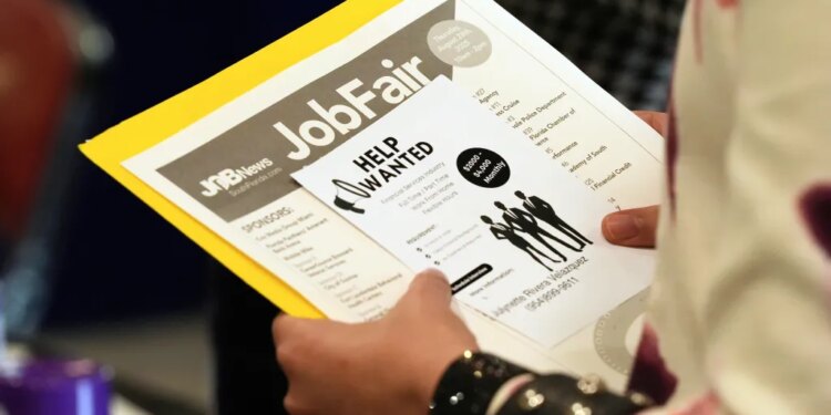 A person holding a flyer for a job fair with "Job Fair" and "Help Wanted" visible.