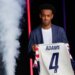 Tyler Adams, a midfielder for the US men's national soccer team, holds up a jersey with "ADAMS" and the number 4 on the back, while being introduced during the 2026 FIFA World Cup roster announcement.