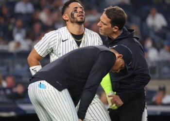 New York Yankees shortstop José Caballero reacts in pain after being hit by a pitch, as manager Aaron Boone and a trainer check on him.