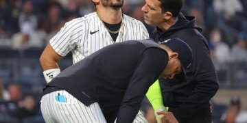 New York Yankees shortstop José Caballero reacts in pain after being hit by a pitch, as manager Aaron Boone and a trainer check on him.