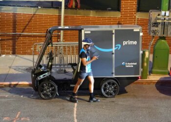 An Amazon Prime delivery driver looks at their phone next to an Amazon Mubea U-Mobility E-Cargobike.