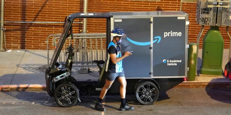 An Amazon Prime delivery driver looks at their phone next to an Amazon Mubea U-Mobility E-Cargobike.