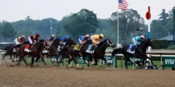 A group of jockeys on horseback race around the first turn of the Belmont Stakes.