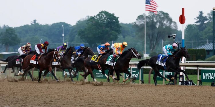 A group of jockeys on horseback race around the first turn of the Belmont Stakes.