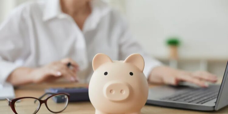 A piggy bank on a desk, with a financial advisor calculating a budget in the background.
