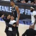 A fan taking a selfie video on the court during the 2026 NBA Finals Game 1 between the New York Knicks and San Antonio Spurs, with players looking on.