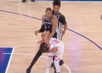 A San Antonio Spurs player falling over an opposing player on the basketball court.
