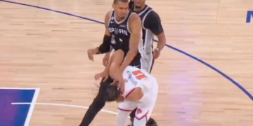 A San Antonio Spurs player falling over an opposing player on the basketball court.