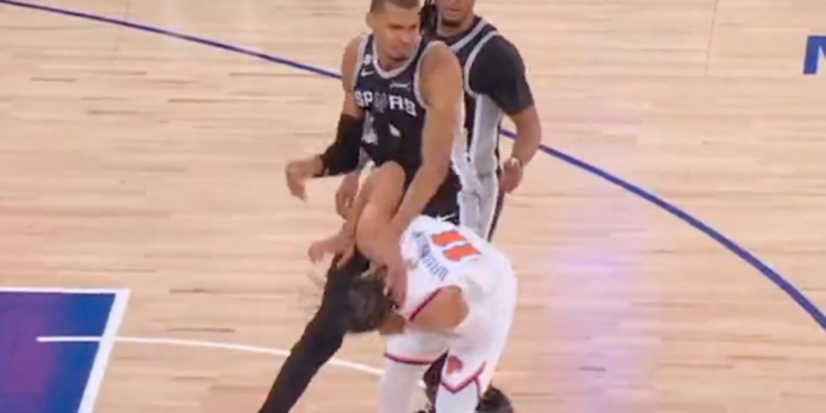 A San Antonio Spurs player falling over an opposing player on the basketball court.