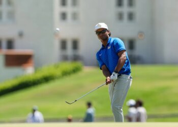 A male golfer in a blue shirt and white hat hitting a golf ball.