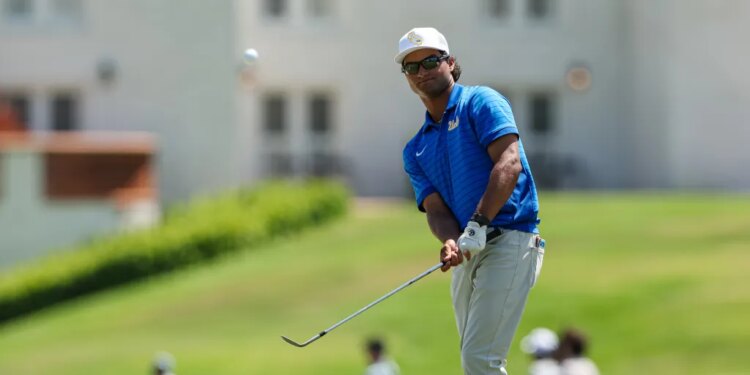 A male golfer in a blue shirt and white hat hitting a golf ball.