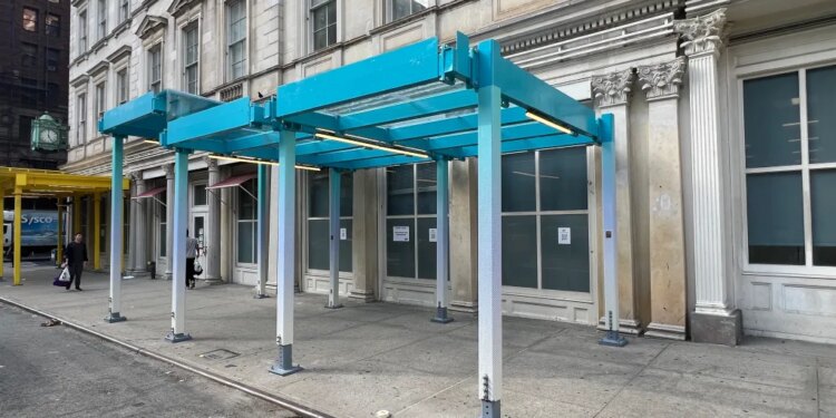 Models of proposed sidewalk sheds in teal and yellow on a city street.