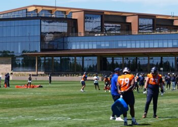 Denver Broncos players practicing football drills in front of the team's new headquarters.