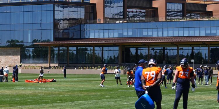 Denver Broncos players practicing football drills in front of the team's new headquarters.