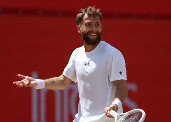 Tennis player Corentin Moutet in a white shirt and wristband, smiling and holding a racket.