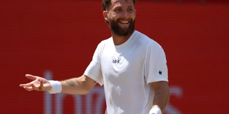 Tennis player Corentin Moutet in a white shirt and wristband, smiling and holding a racket.