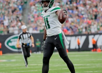 A football player in a green and white uniform holds a football on the field.