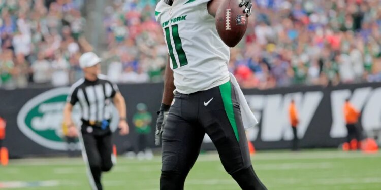 A football player in a green and white uniform holds a football on the field.