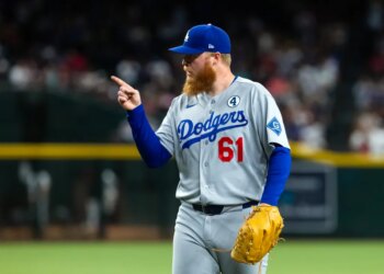 Los Angeles Dodgers player in gray uniform and blue cap pointing with right hand.
