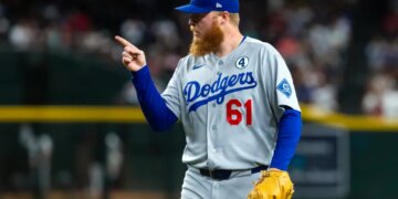Los Angeles Dodgers player in gray uniform and blue cap pointing with right hand.