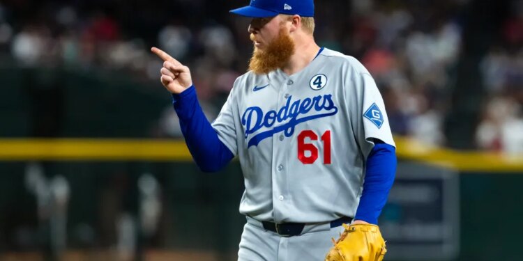 Los Angeles Dodgers player in gray uniform and blue cap pointing with right hand.