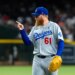 Los Angeles Dodgers player in gray uniform and blue cap pointing with right hand.