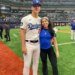 Bobby Miller, wearing a Dodgers uniform, and Natalie Loureda, in a blue shirt, smiling on a baseball field.