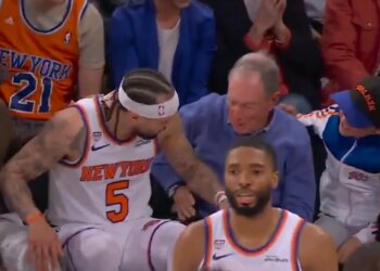 New York Knicks player number 5 falling into the stands and interacting with a man in a blue sweater.