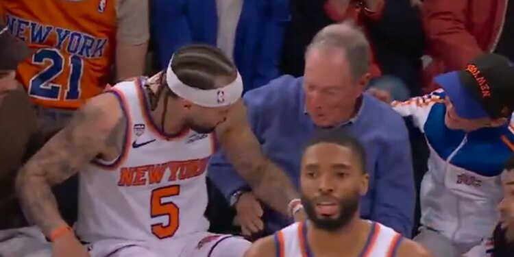 New York Knicks player number 5 falling into the stands and interacting with a man in a blue sweater.