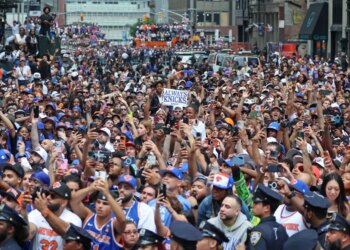 Crowds of fans wearing New York Knicks gear celebrate at a ticker-tape parade in Lower Manhattan.