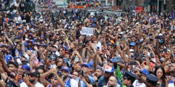 Crowds of fans wearing New York Knicks gear celebrate at a ticker-tape parade in Lower Manhattan.