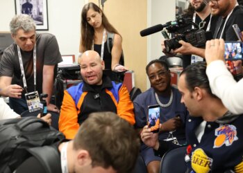 Rapper Fat Joe in a blue jacket and a black New York Knicks hat, yelling courtside at an NBA Finals game.