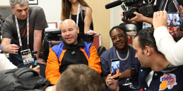 Rapper Fat Joe in a blue jacket and a black New York Knicks hat, yelling courtside at an NBA Finals game.