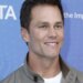 Tom Brady smiling while wearing a light brown jacket over a white shirt.