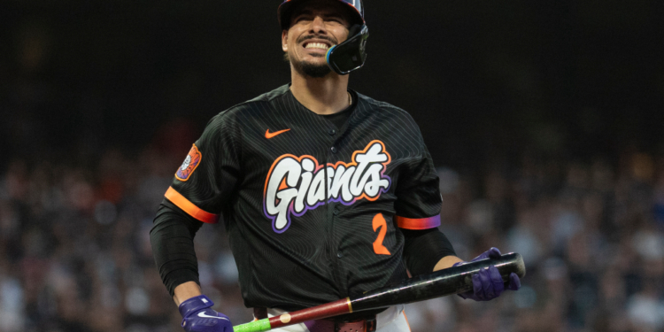 A baseball player for the San Francisco Giants, wearing a black jersey with orange and purple lettering, holds a bat and smiles.
