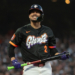 A baseball player for the San Francisco Giants, wearing a black jersey with orange and purple lettering, holds a bat and smiles.
