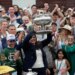 Trainer Cherie DeVaux holds the trophy aloft, flanked by jockey Jose Ortiz and cheered on by a crowd.