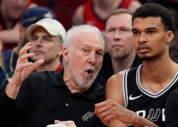 San Antonio Spurs coach Gregg Popovich talking with Victor Wembanyama on the bench.