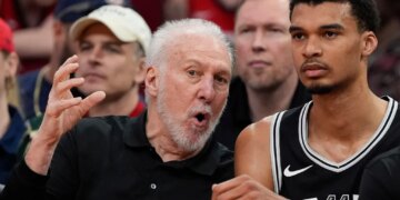 San Antonio Spurs coach Gregg Popovich talking with Victor Wembanyama on the bench.