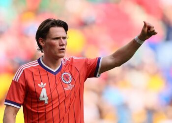 Scotland's Scott McTominay in a red jersey, raising his arm on a colorful field.