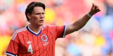 Scotland's Scott McTominay in a red jersey, raising his arm on a colorful field.