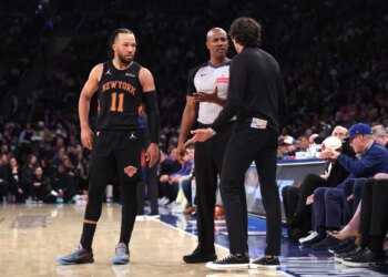 Knicks guard Jalen Brunson observes as Atlanta Hawks head coach Quin Snyder disputes a call with a referee.