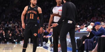 Knicks guard Jalen Brunson observes as Atlanta Hawks head coach Quin Snyder disputes a call with a referee.