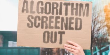 A hand holding up a cardboard sign that says "ALGORITHM SCREENED OUT" in capital letters.
