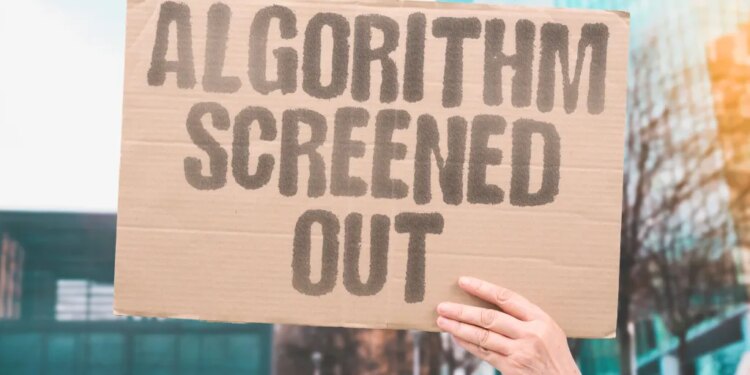A hand holding up a cardboard sign that says "ALGORITHM SCREENED OUT" in capital letters.