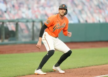 A San Francisco Giants baseball player on a base, wearing an orange jersey with "Giants" written across the chest and a black batting helmet.