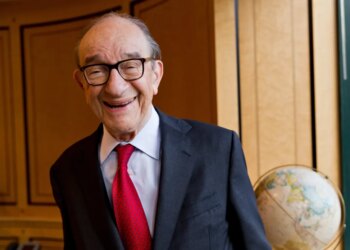 Economist Alan Greenspan smiles, wearing glasses, a suit jacket, and a red tie.